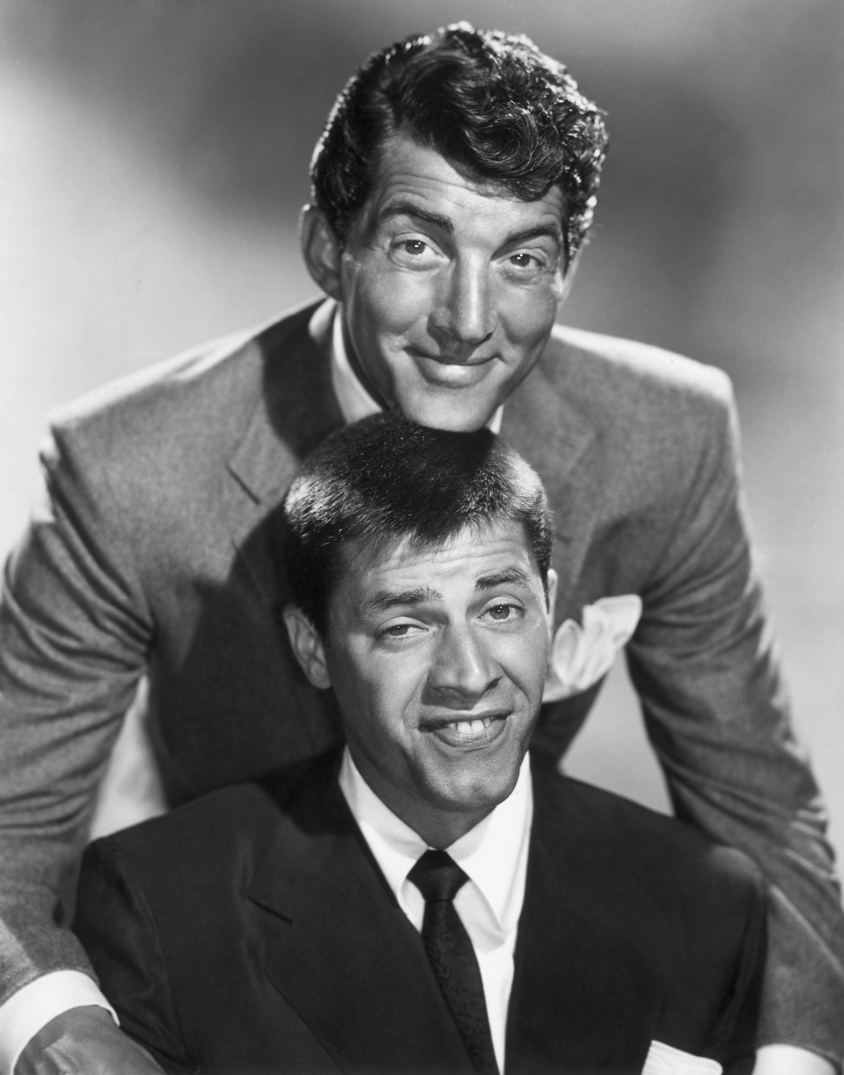 circa 1955: American comic team Dean Martin (1917 - 1995) and Jerry Lewis smiling in a promotional portrait. Martin smiles and rests his chin on top of Lewis's head, as Lewis makes a funny face.